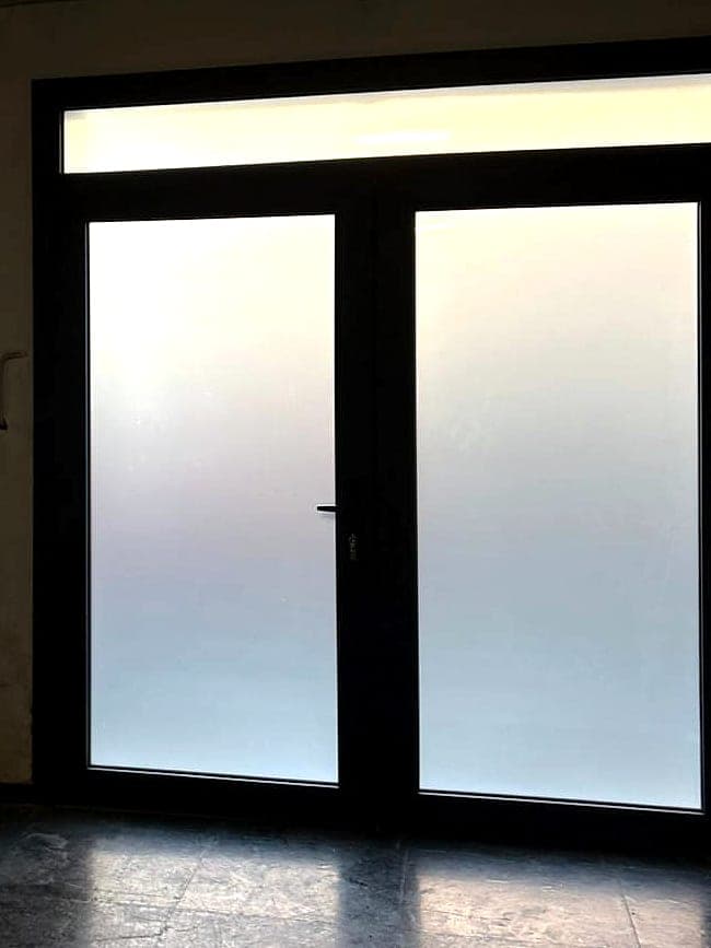 Porta d'ingresso a due ante con telaio scuro, vetri satinati e sopraluce, nell'androne di un palazzo
