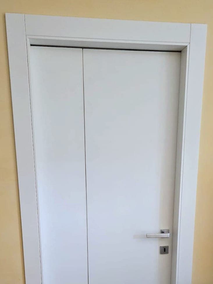 Porta interna a battente bianca con incisione verticale decorativa e maniglia in metallo satinato