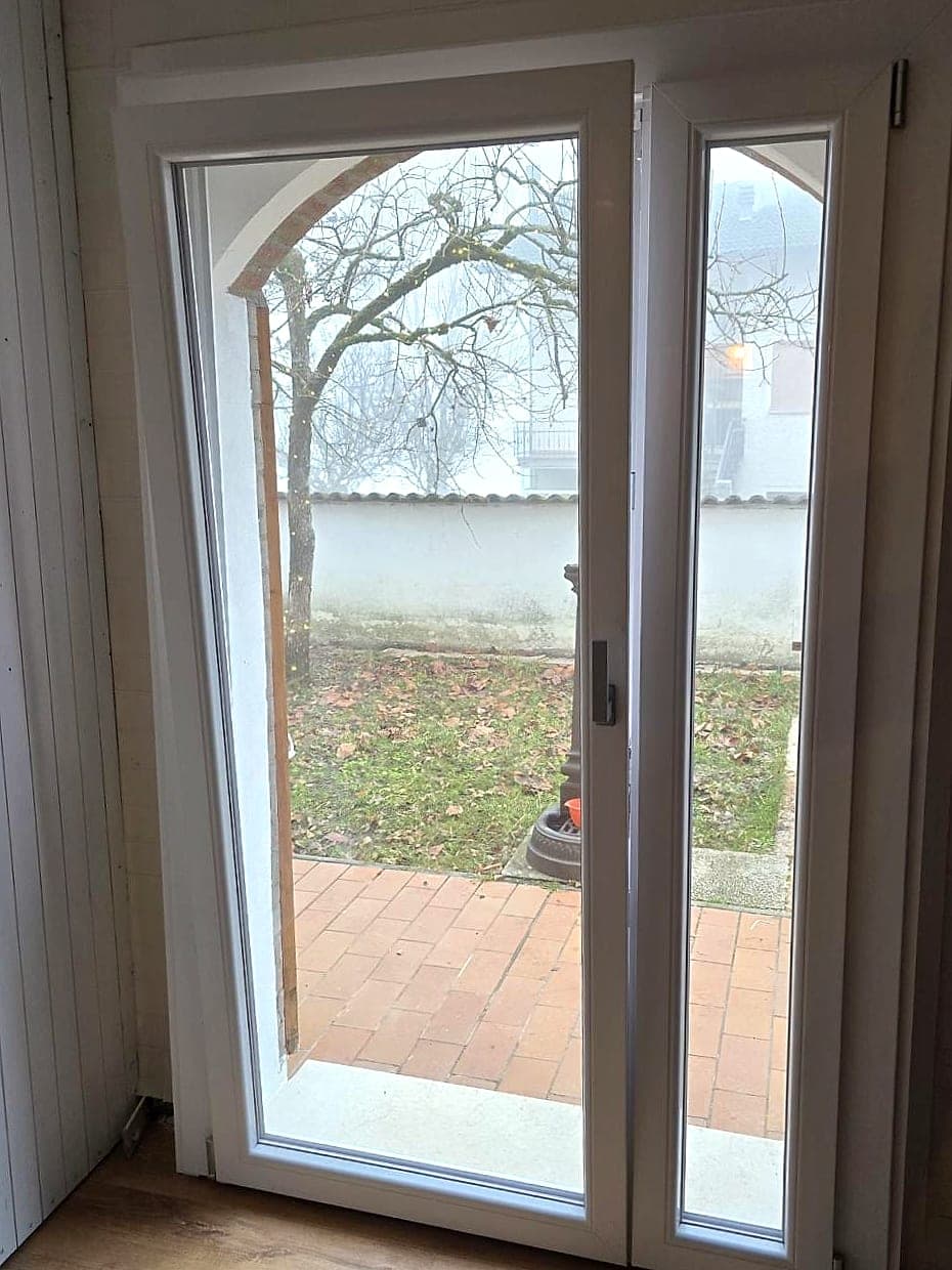 Portafinestra ad arco a due ante in bianco, vista dall'interno verso il cortile